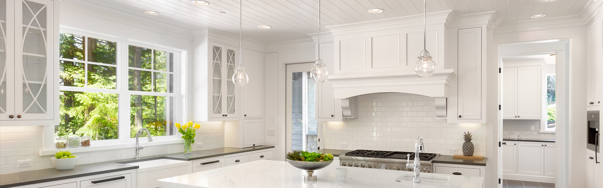 The sun shines through a kitchen casement window into a modern white marble kitchen.